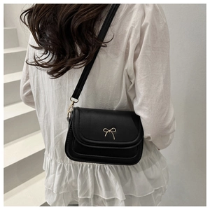 Fashionable black crossbody bag with gold bow clasp shown on a model against white stairs