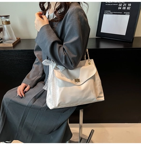 Détail du sac bandoulière blanc avec bordure en dentelle, nœud et fermoir doré rotatif
