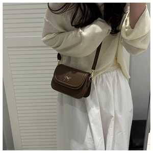 Detail of dark brown leather crossbody bag with a gold bow accent and slim strap
