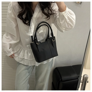 Minimalist black matte leather bucket bag with gold ring hardware shown on a model