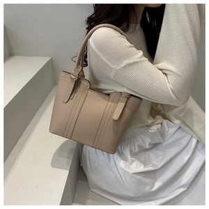 Detailed close-up of the beige leather tote bag featuring golden metal ring handles