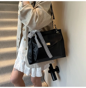 Détail du sac à bandoulière noir avec fermoir doré et ruban de dentelle blanche