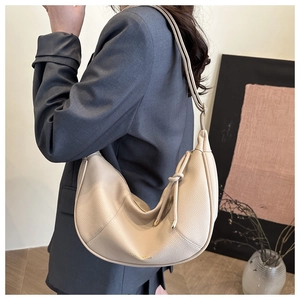 Detail view of beige pebbled leather dumpling bag on model with elegant knot accent