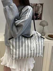 Black and white striped canvas tote bag with lace bow decoration worn by model