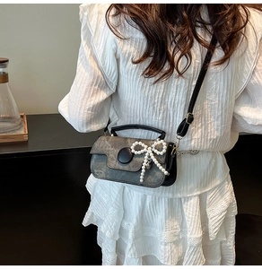 Détail d'un sac bandoulière rétro avec nœud perlé et sangle noire porté par un mannequin