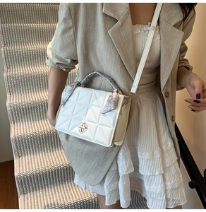 Close-up of quilted beige crossbody bag with gold twist lock and silk scarf handle