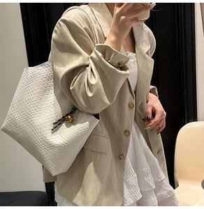 Détail du sac cabas blanc tissé avec breloque boule dorée et bandoulière tressée