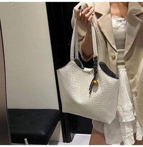 Détail du sac cabas beige tressé avec breloque à perle dorée et texture en cuir mat