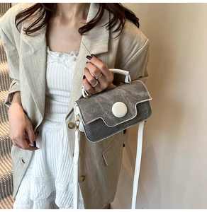 Petit sac texturé gris avec détails contrastés blancs porté par un mannequin en costume beige