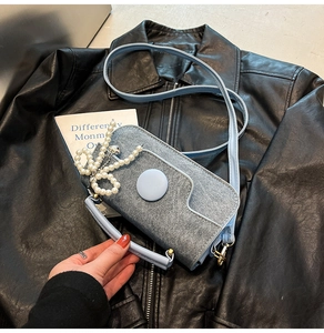 Détail du mini sac bleu texturé avec perle et pendentif cœur sur fond de cuir noir