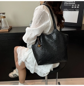 Détail du sac cabas tressé noir en cuir brillant avec pendentif métallique décoratif