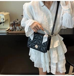 Detail of black quilted shoulder bag with silver lock and silk scarf on white dress