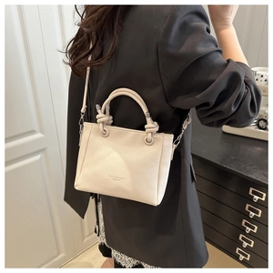 Détail du sac bandoulière carré en cuir crème avec poignées nouées et texte embossé