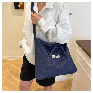 Detail of dark blue denim crossbody bag with decorative bow and stylish logo patch