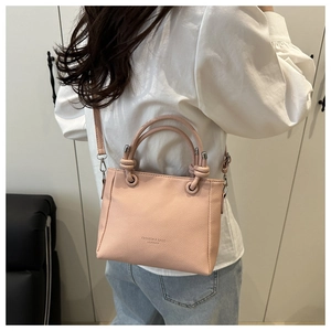 Détail du sac seau en cuir rose porté avec une chemise blanche et un jean bleu