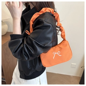 Detail of bright orange shoulder bag featuring white bow embroidery and pleated cloud strap