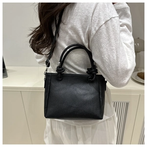 Détail du sac seau noir en cuir grainé avec poignée nouée et boucle argentée sur modèle