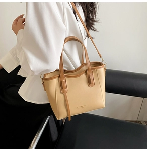 Detail view of beige and brown leather bucket bag worn by a model in a white shirt