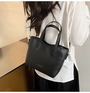 Detail of a black leather bucket bag with gold lettering and detachable shoulder strap