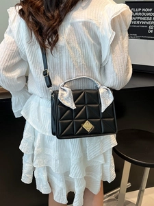Black quilted crossbody bag with silk scarf handle on a model wearing a white dress