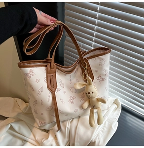 Detail of tote bag with graffiti prints, brown leather handles and rabbit charm