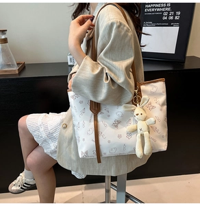 Detail view of white tote bag with brown leather trim and cute rabbit plush charm