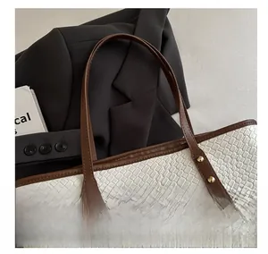 Detail of white woven tote bag with brown leather handles and gold rivet accents