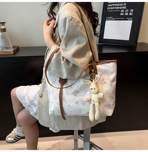 Close-up of white graffiti tote bag with brown straps and a cute plush bunny pendant