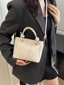 Sac seau tendance en cuir blanc cassé porté en bandoulière par un mannequin en intérieur