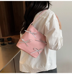 Pink bucket bag with silver bow accents shown on shoulder for a stylish look