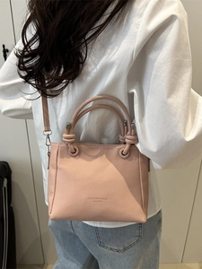 Sac seau rose pâle en cuir grainé avec anse nouée porté par un mannequin au style urbain