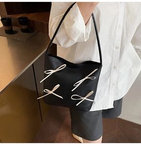 Detail of a black leather bucket bag featuring four elegant white bow decorations
