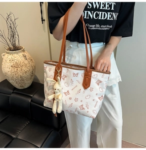Close-up of white tote bag featuring bear and butterfly prints with a plush bunny charm