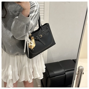 Detailed view of black leather tote bag featuring white stitching and silk scarf accessory
