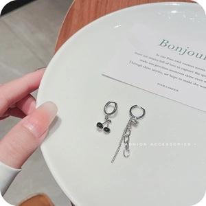Asymmetric silver cherry earrings with black heart charms and chain on a ceramic plate