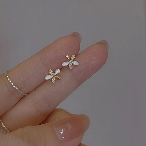 Detailed macro view of delicate gold flower earrings with white enamel and micro diamonds