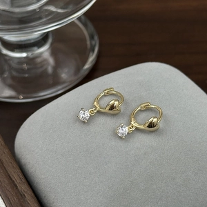 Detail of gold heart earrings with zircon charms on a textured display background
