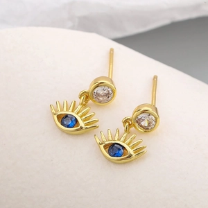 Boucles d'oreilles œil protecteur dorées avec zircons bleus sur fond de pierre blanche