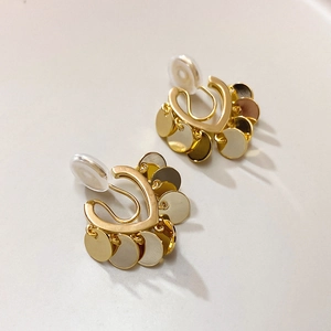Orecchini a clip dorati con base a cuore e paillettes metalliche su uno sfondo caldo