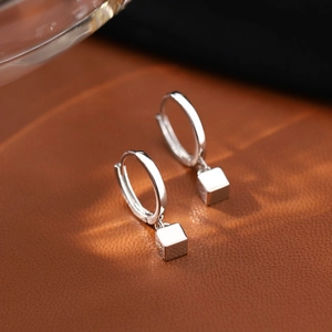 Detail of geometric square charms on S925 silver hoop earrings with a polished finish