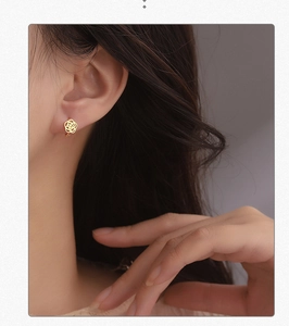Close-up of elegant gold hollow rose stud earrings worn on a female model's ear