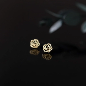Macro shot of gold hollow rose earrings on a reflective black background with soft lighting