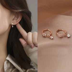 Close-up of rose gold flower earrings with zircon drop on silk and mesh background