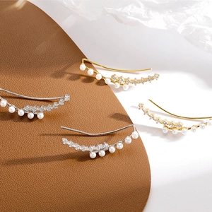 Elegant gold and silver ear crawlers with pearls and zircon on a textured background
