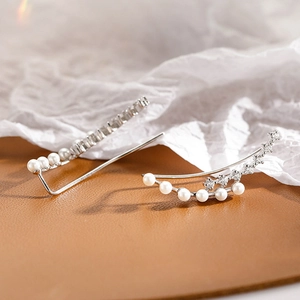 Detail of silver pearl ear crawlers with zircon accents on leather and paper background