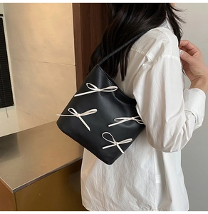 Side view of black faux leather shoulder bag with white ribbon bows on model