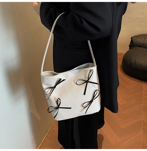 Close-up of a white leather underarm bag with black bow accents on a female model