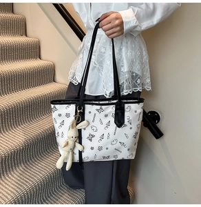 Close-up of white graffiti tote bag with black handles and cute plush bunny pendant