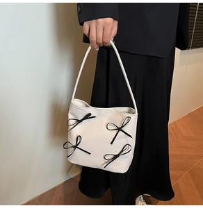 Detailaufnahme der weißen Beuteltasche mit schwarzen Schleifen und glattem Kunstleder