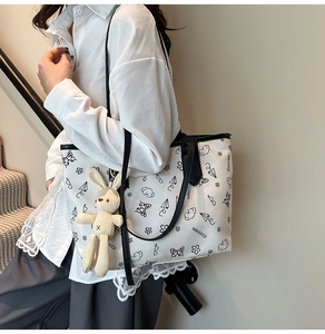 Detail of white tote bag with black doodle prints and a beige plush bunny keychain